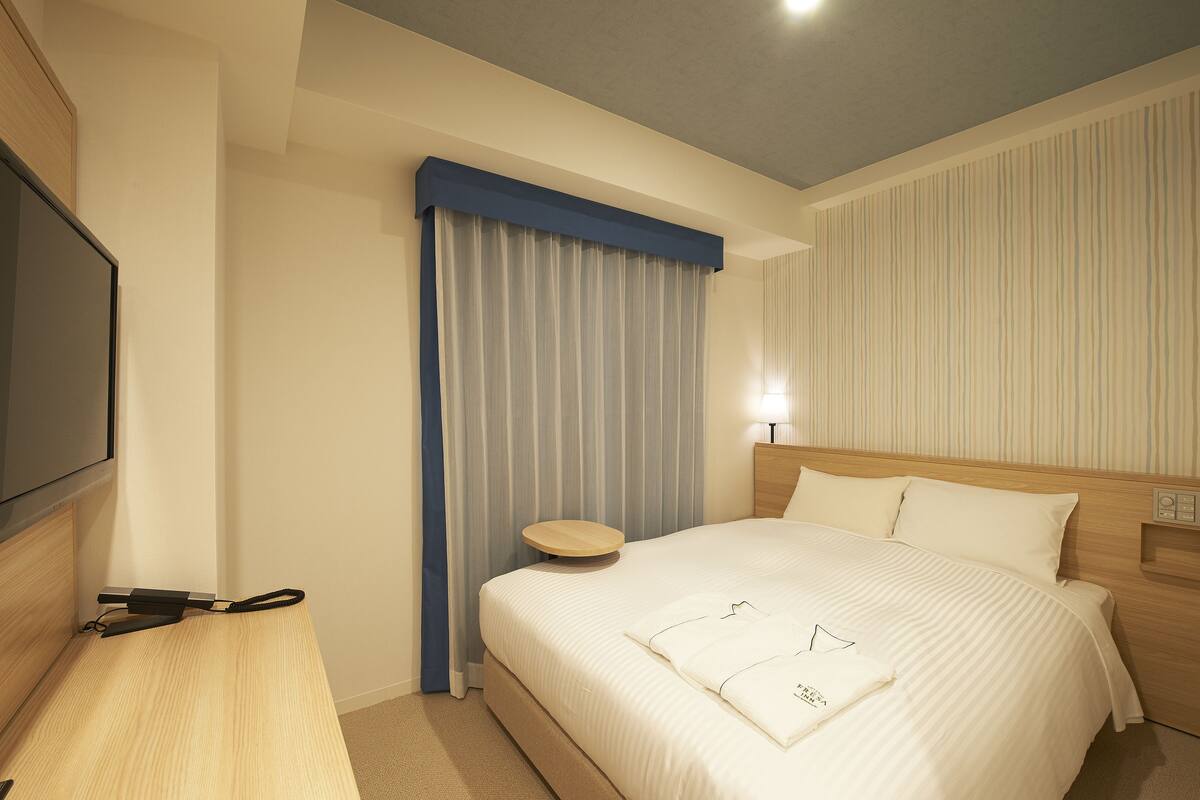 Ein Hotelzimmer mit Bett, Flachbildfernseher, Nachttisch und Vorhang.