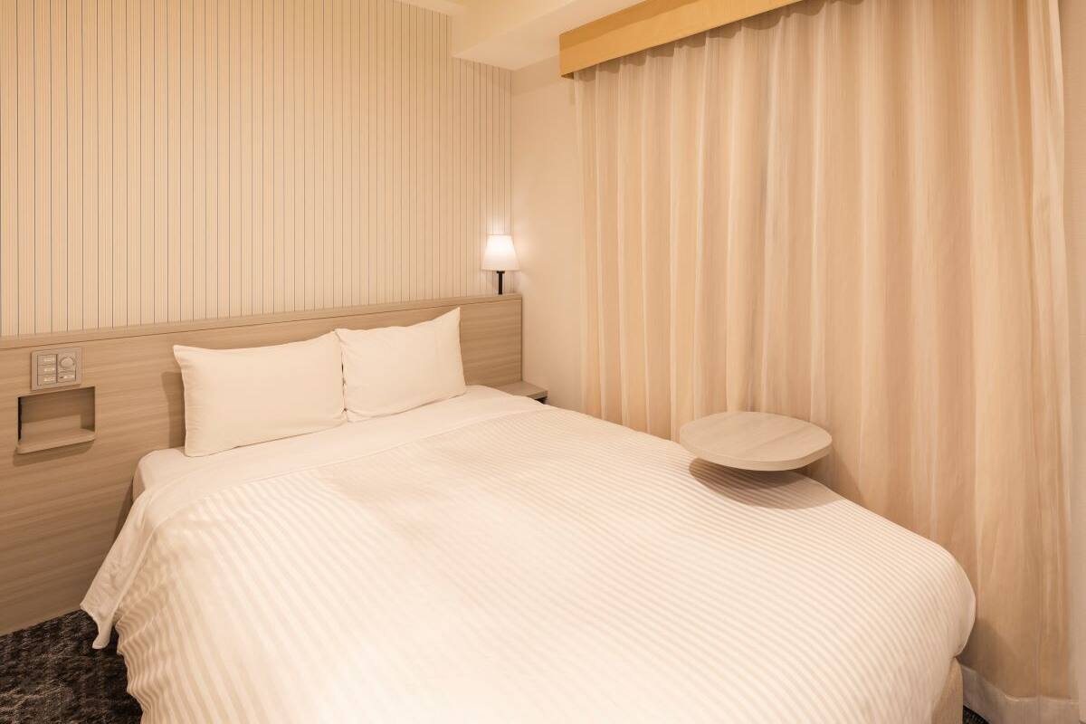 Ein Hotelzimmer mit einem großen Bett, einem Nachttisch, einer Lampe und einem Fenster mit Vorhängen.