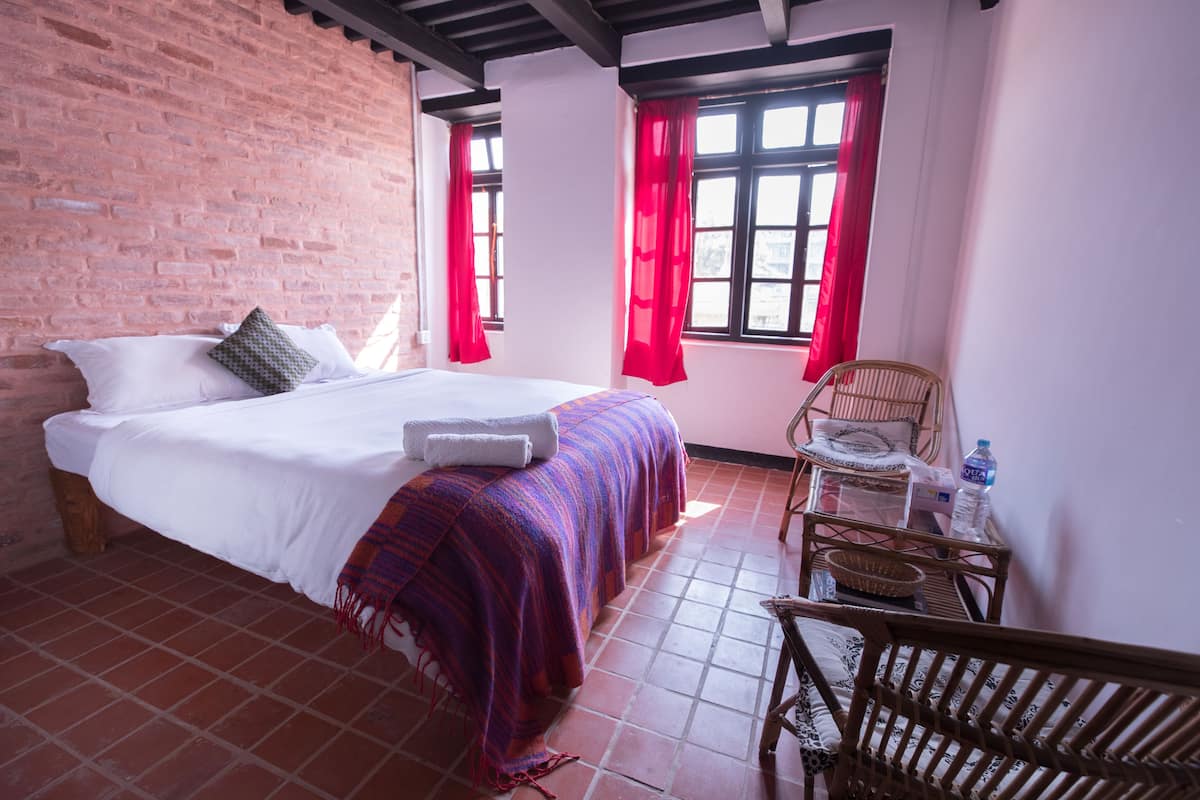 A room with a bed, a chair, a table, and a window with red curtains.