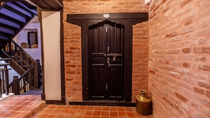 Un muro de ladrillo con una puerta de madera oscura y una lámpara de aceite de bronce en el suelo.