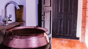 Un baño rústico con un lavabo de cobre, un estante de madera y una puerta negra que da a una zona de ladrillo.