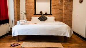 Una cama bien hecha con una colcha blanca, un cojín decorativo y una mesita de noche con un florero y un libro.