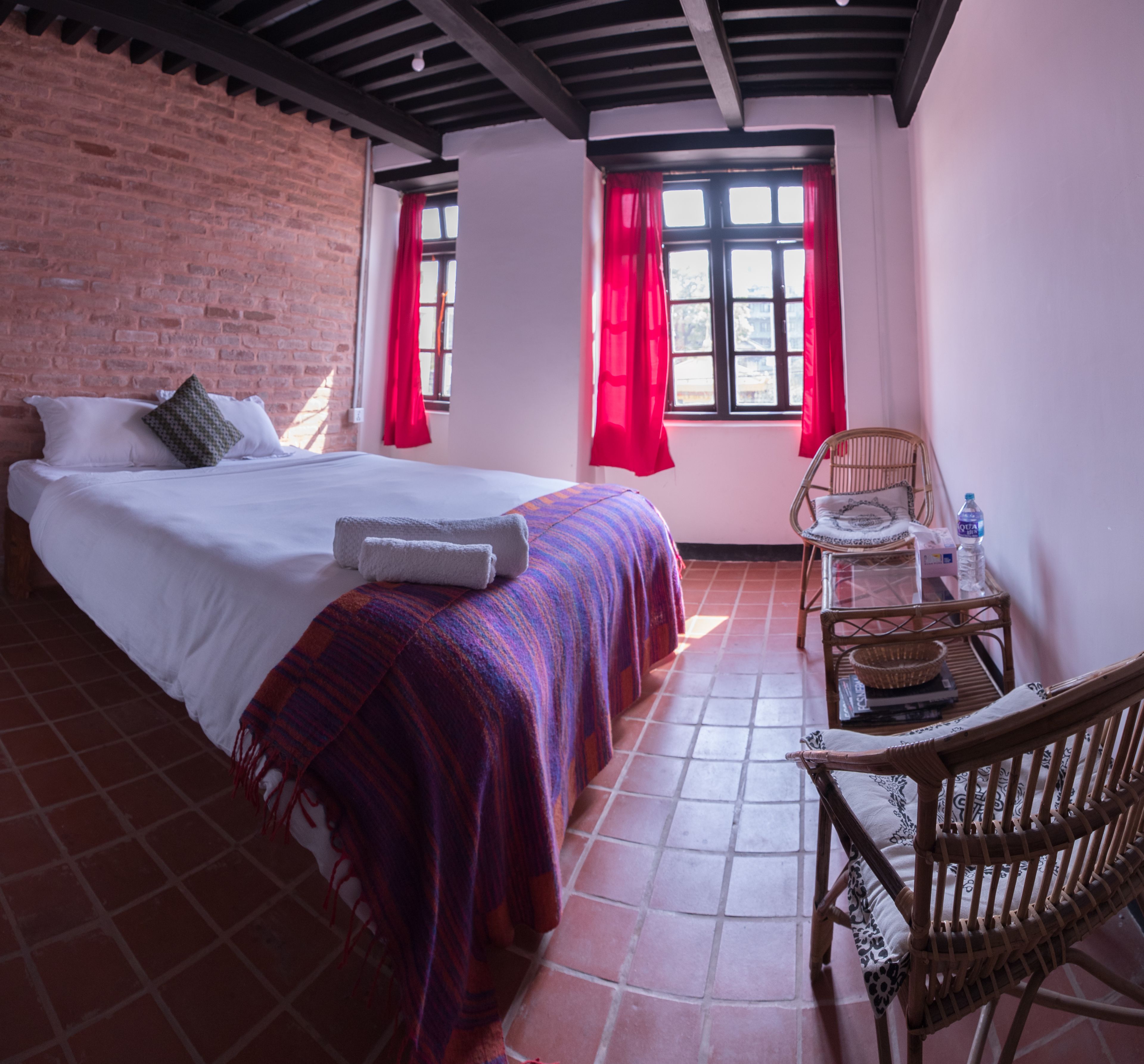 A hotel room with a bed, a chair, a table, and a window with curtains.
