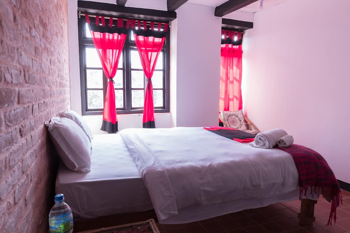 A double bed with white linens, a red and black checkered blanket, and a water bottle on the nightstand.