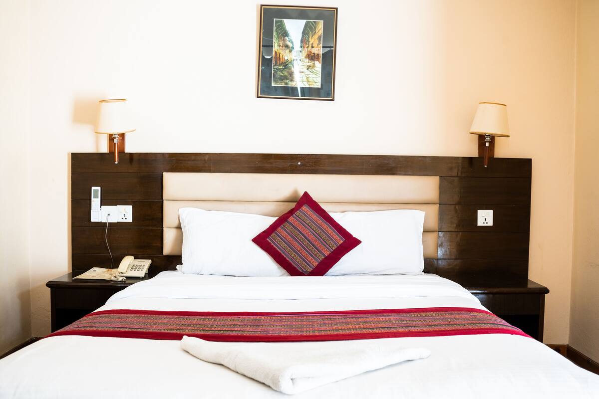 A hotel room with a neatly made bed, a bedside table with a lamp, and a wall-mounted picture.