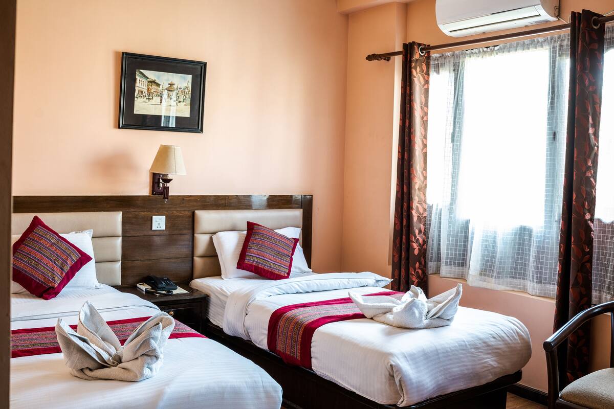 A hotel room with two beds, a framed picture on the wall, a bedside lamp, and a window with curtains.