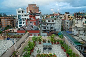 A rooftop terrace with potted plants and a table, surrounded by multi-story buildings. - Hotel Namtso (Kathmandu)