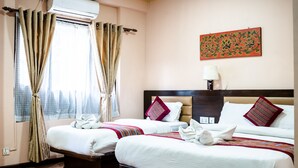A hotel room with two beds, a window with curtains, a wall-mounted air conditioner, a nightstand with a lamp, and a decorative wall piece. - Hotel Namtso (Kathmandu)