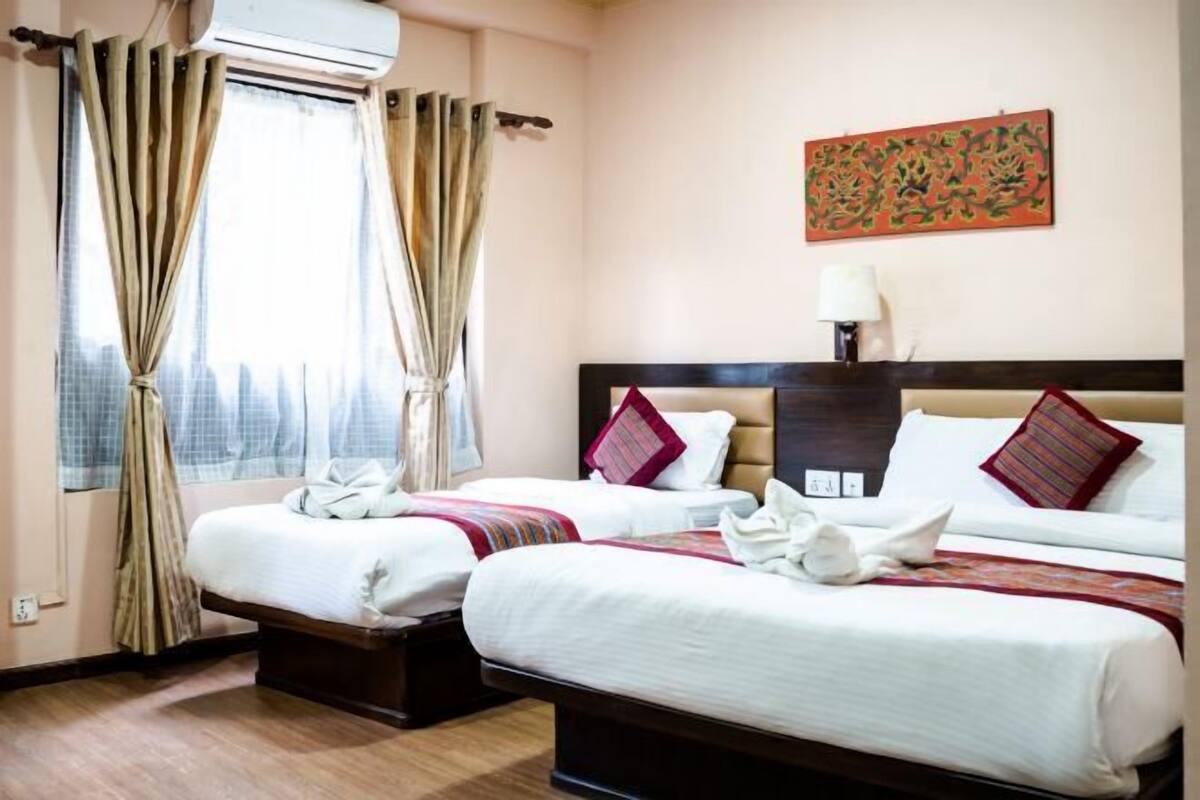 A hotel room with two beds, a window with curtains, a wall-mounted air conditioner, and a painting.