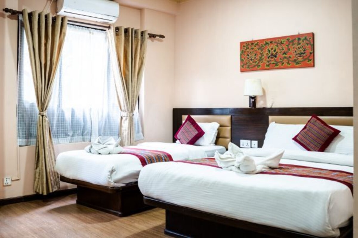 A hotel room with two beds, a window with curtains, a wall-mounted air conditioner, and a painting.