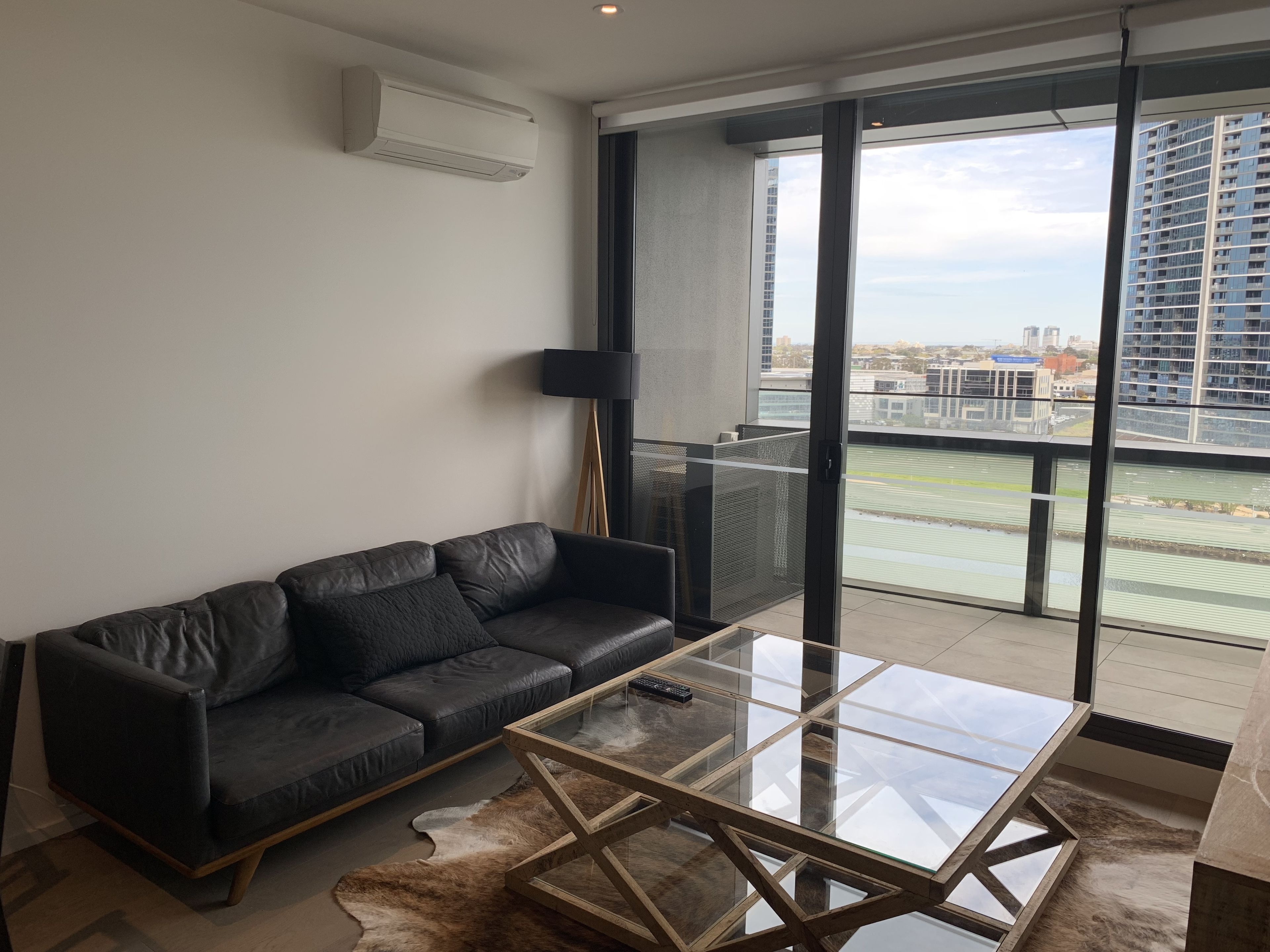 A modern living room with a leather sofa, a glass coffee table, and a view of a cityscape through large windows.