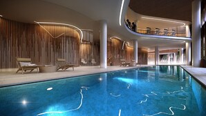 Un espace piscine intérieur moderne, doté d’une piscine à eau claire, de chaises longues et d’un espace de détente à plusieurs niveaux offrant une vue sur la piscine.