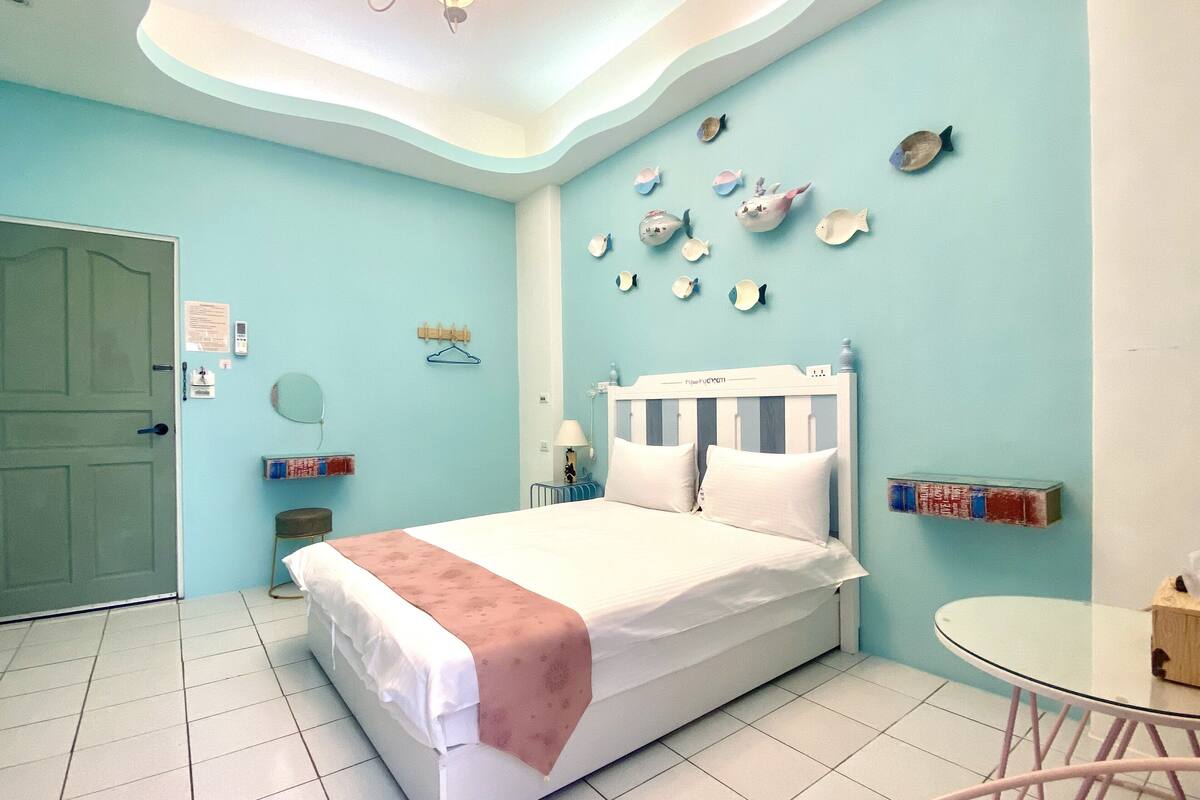 Quarto com cama, mesa de cabeceira, cadeira, mesa redonda e parede decorada com peixes.