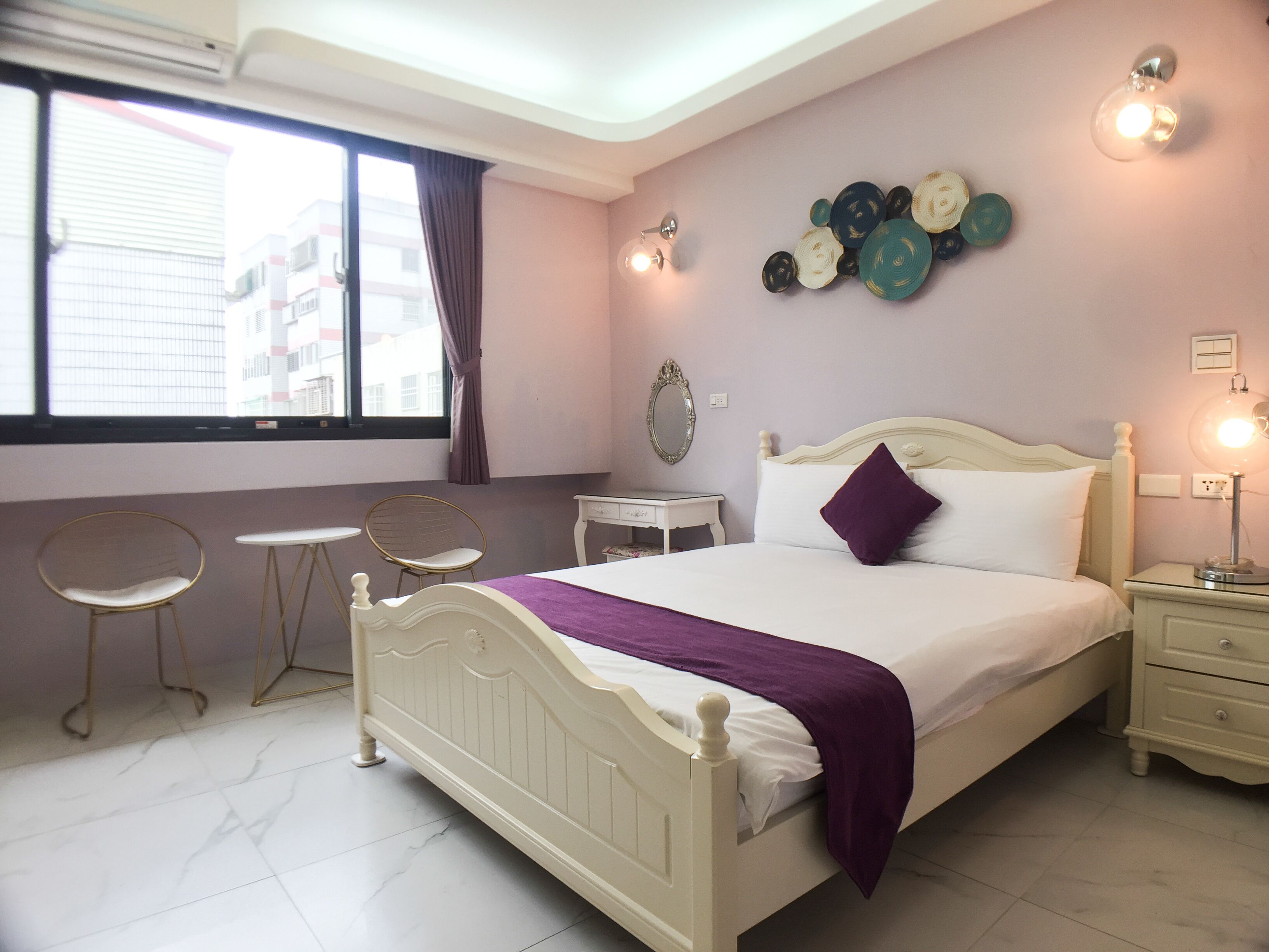 Un dormitorio con cama, mesitas de noche, una silla, un espejo y una decoración en la pared.