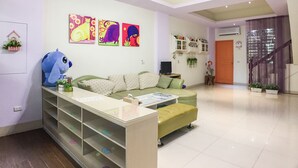 Un salon avec un canapé vert, un jouet en peluche bleu et des œuvres d’art colorées accrochées au mur.