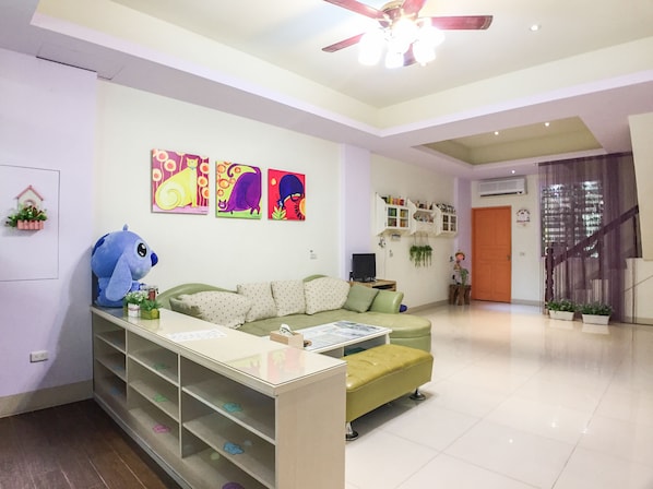 Un salon avec un canapé vert, un jouet en peluche bleu et des œuvres d’art colorées accrochées au mur.
