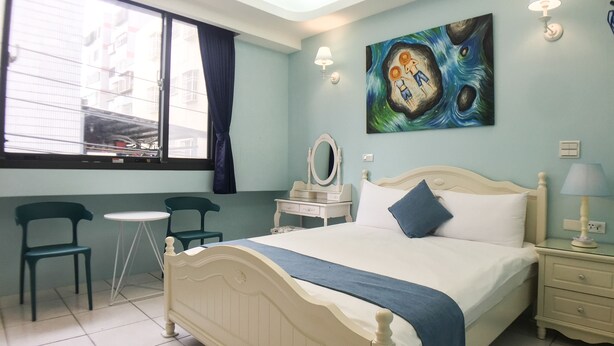 Une chambre d’hôtel avec un lit, un bureau, deux chaises, une fenêtre et des œuvres d’art accrochées au mur.