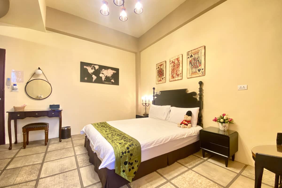 Quarto bem organizado com cama, mesa de cabeceira, abajur e pequena escrivaninha com cadeira.