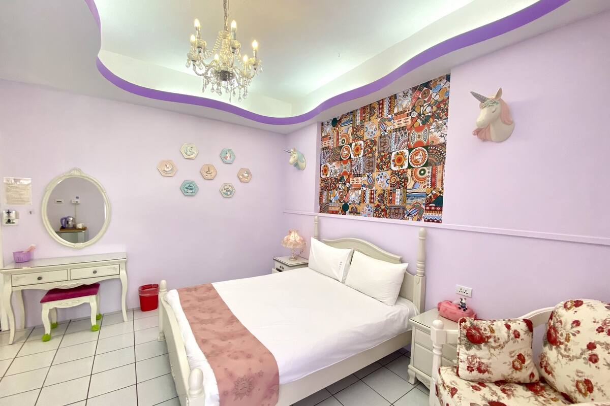 Quarto com cama, cômoda, penteadeira, cadeira e parede decorada com tapeçaria e um unicórnio.