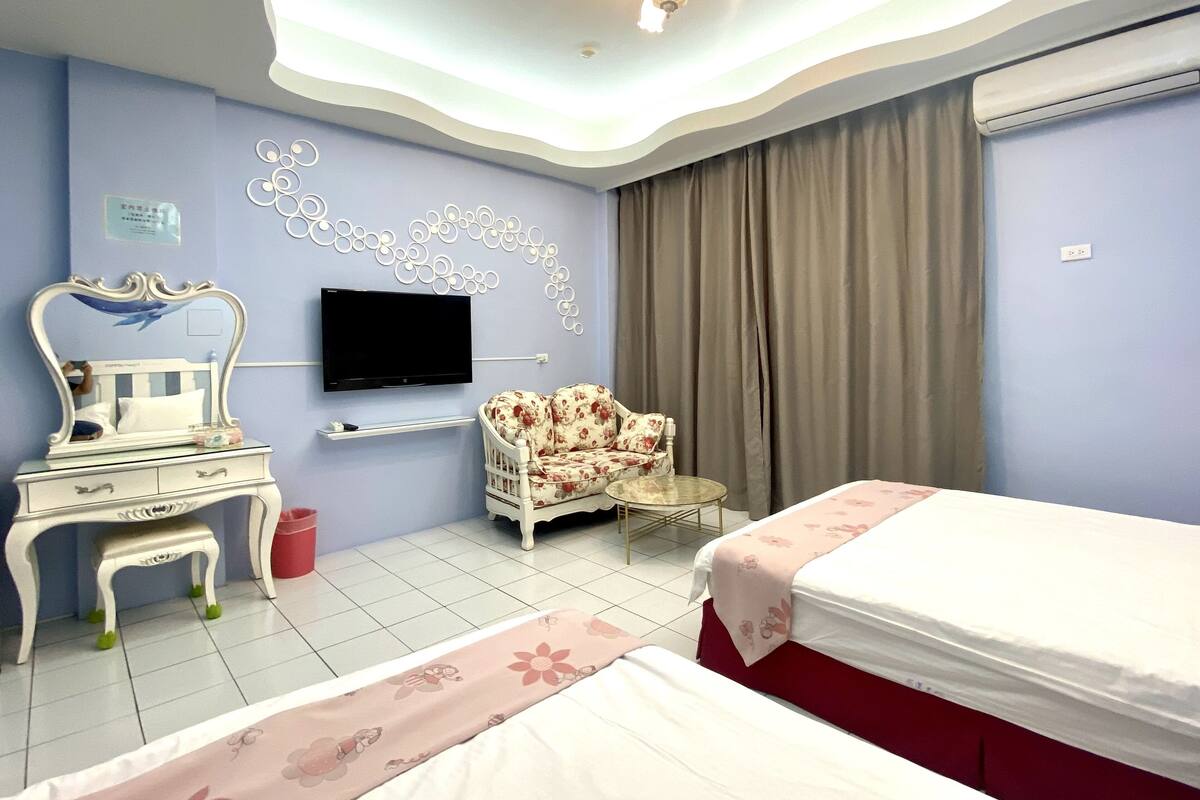 Quarto de hotel com cama, cadeira, toucador com espelho, televisão de tela plana na parede e luminária no teto.