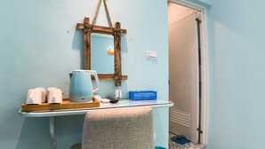 Une salle de bain avec un mur bleu clair, un porte-serviettes en bois, un miroir, une bouilloire, un panier bleu et une serviette sur le sol.