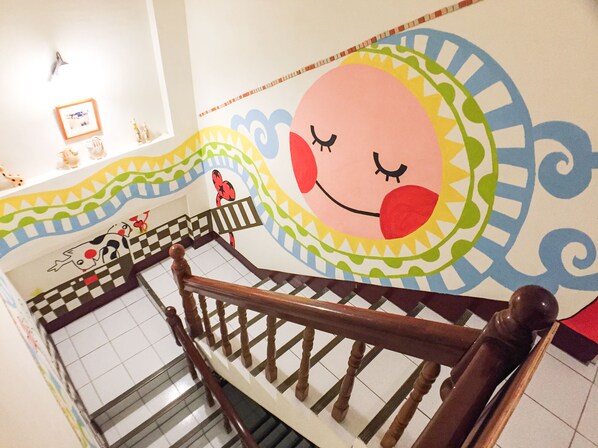 Una escalera con barandilla de madera y un mural colorido en la pared.