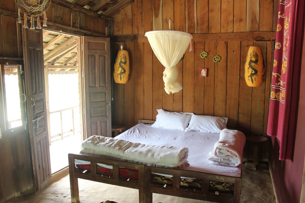 Quarto de madeira com uma cama, mosquiteiro pendurado e porta de madeira.