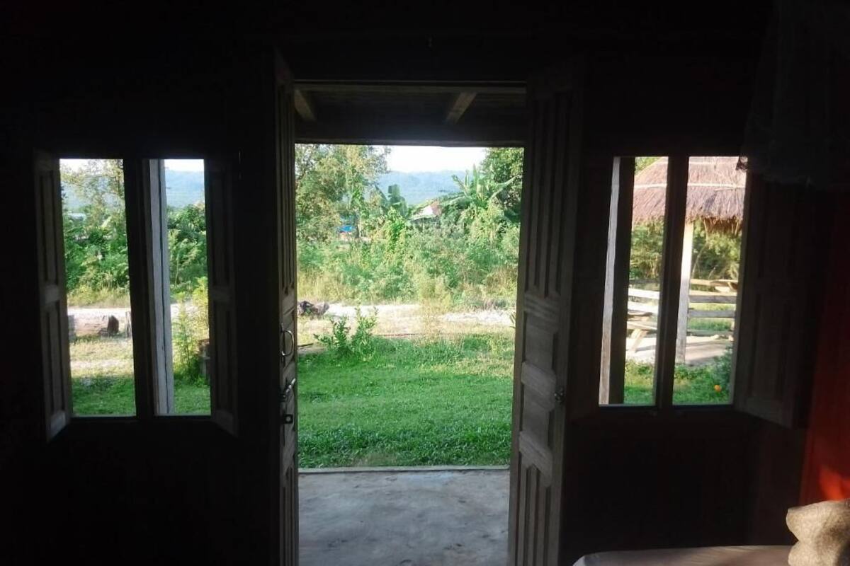 Abertura de porta que dá para um espaço gramado com caminho de concreto, cercado por vegetação e uma montanha ao longe.