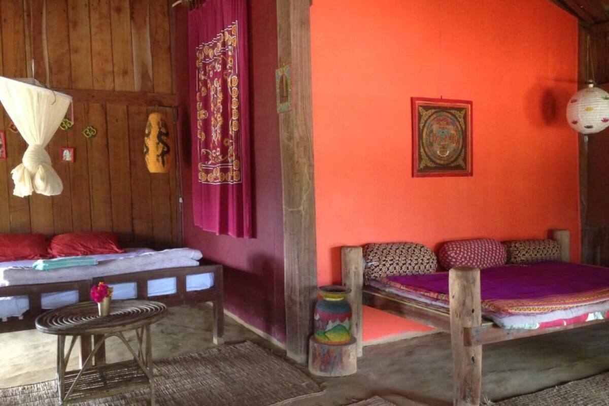 Quarto com cama, uma pequena mesa, luminária pendente e um quadro na parede.
