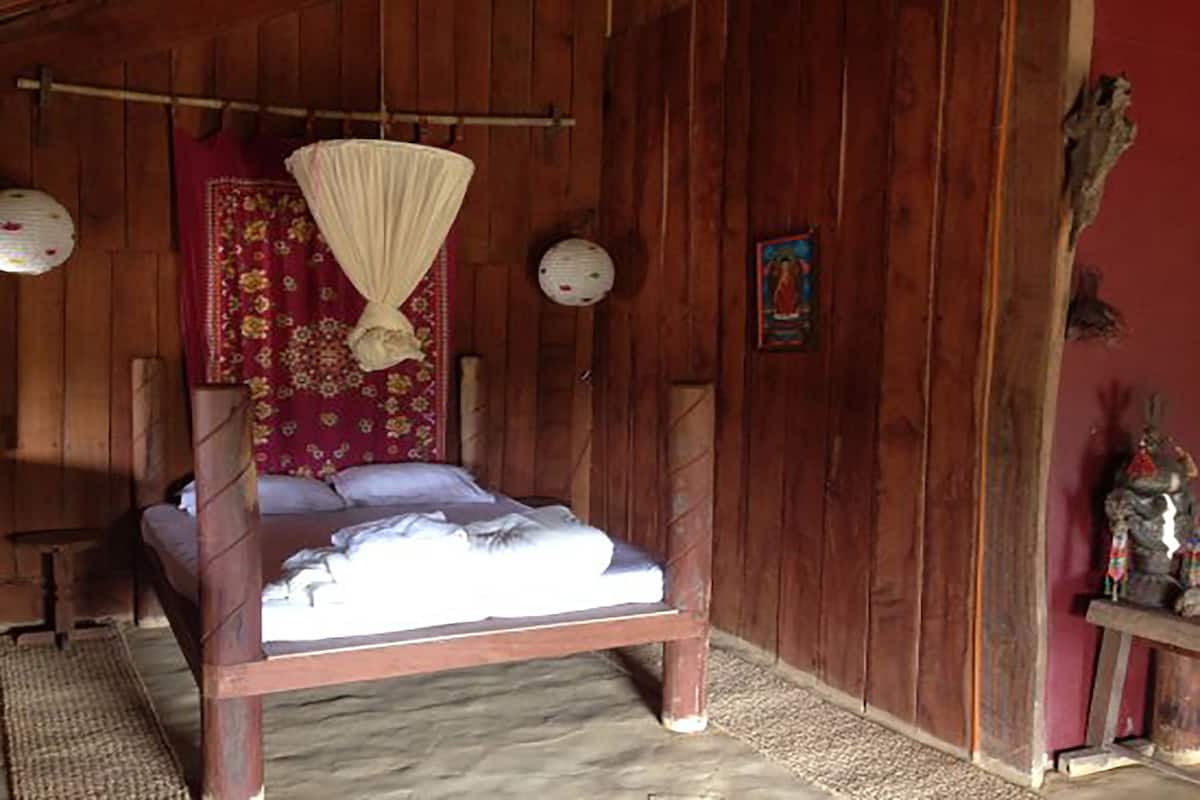 Quarto de madeira com uma cama, mosquiteiro suspenso e um objeto decorativo na parede.