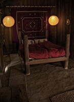 Una habitación rústica de madera con una cama, dos faroles de papel colgantes y un tapiz decorativo en la pared.