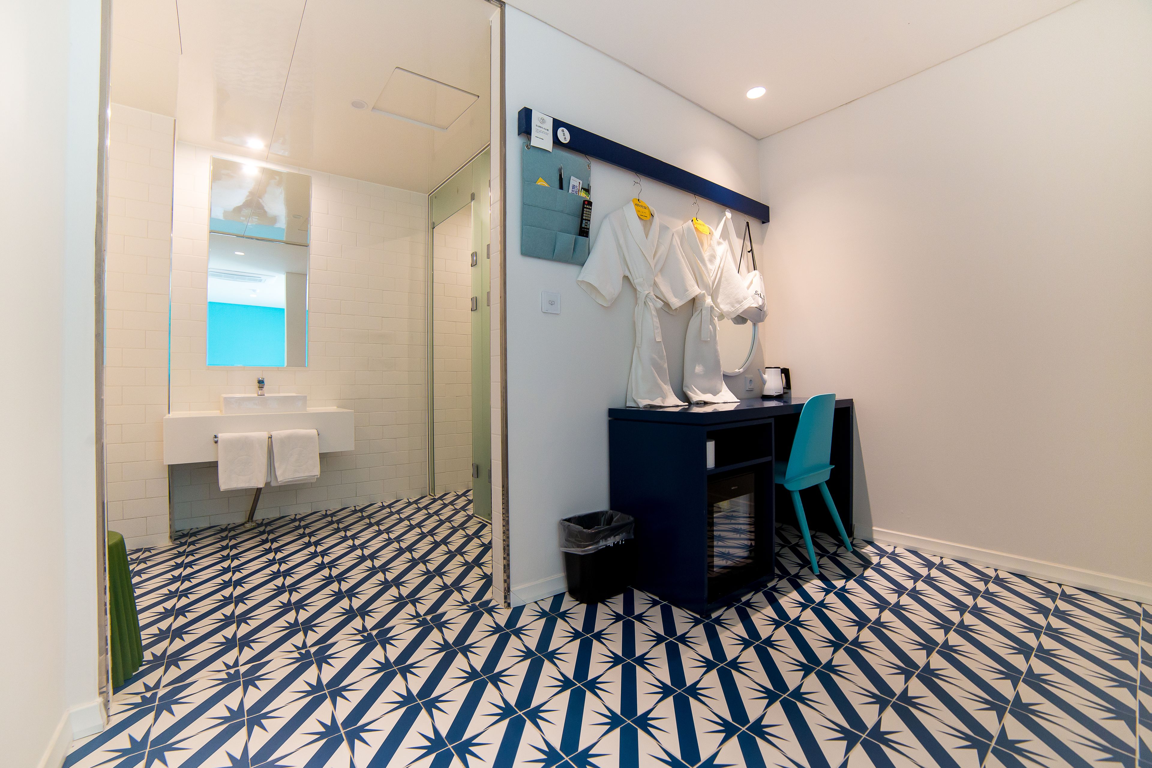 A modern bathroom with a geometric tile floor, a mirror, a sink, and a blue cabinet with towels and robes.