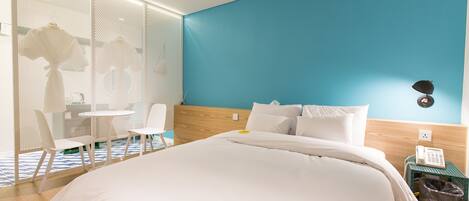 Habitación de hotel con cama, sillas blancas, una mesita pequeña, teléfono y un cubo de basura.