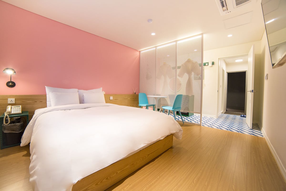 A hotel room with a large bed, a desk with a chair, a small table, and a partition wall.
