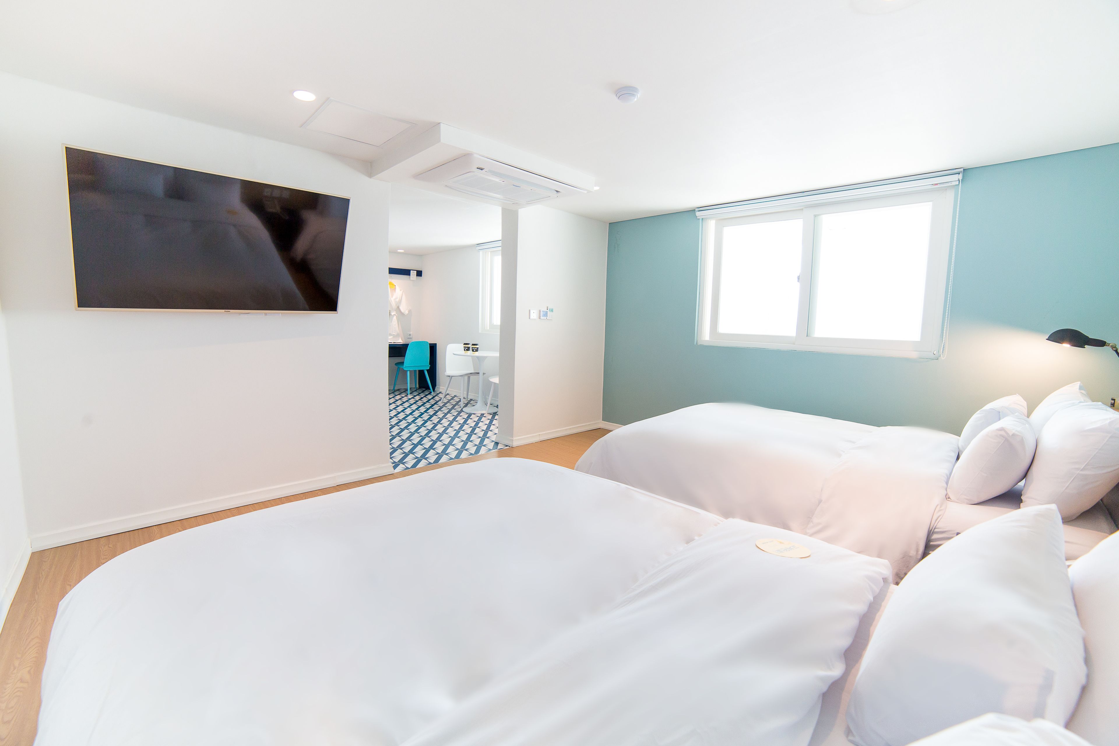 A hotel room with two beds, a TV mounted on the wall, a window, and a bathroom visible in the background.