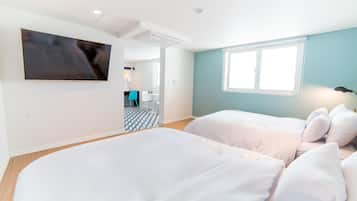 A hotel room with two beds, a TV mounted on the wall, a window, and a bathroom visible in the background.