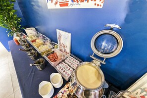 Un montaje tipo bufé con diversos recipientes de comida y una cafetera grande.