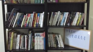 Une bibliothèque remplie de livres et de DVD, un sac Starbucks et une boîte en carton ornée d’un dessin représentant un pouce levé.
