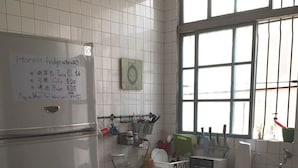 Une cuisine avec un réfrigérateur blanc, une fenêtre à barreaux et un panneau indiquant les prix des boissons.