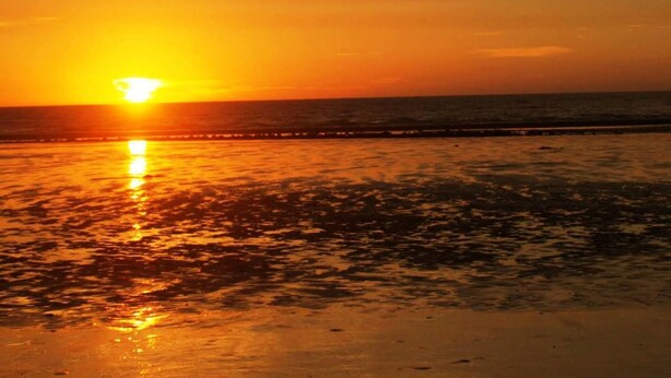 Un coucher de soleil sur une plage, avec une jetée qui s’avance dans l’eau.
