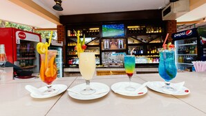 Een barruimte met vier kleurrijke cocktails op witte borden, een Coca-Cola koelkast en een Pepsi koelkast.