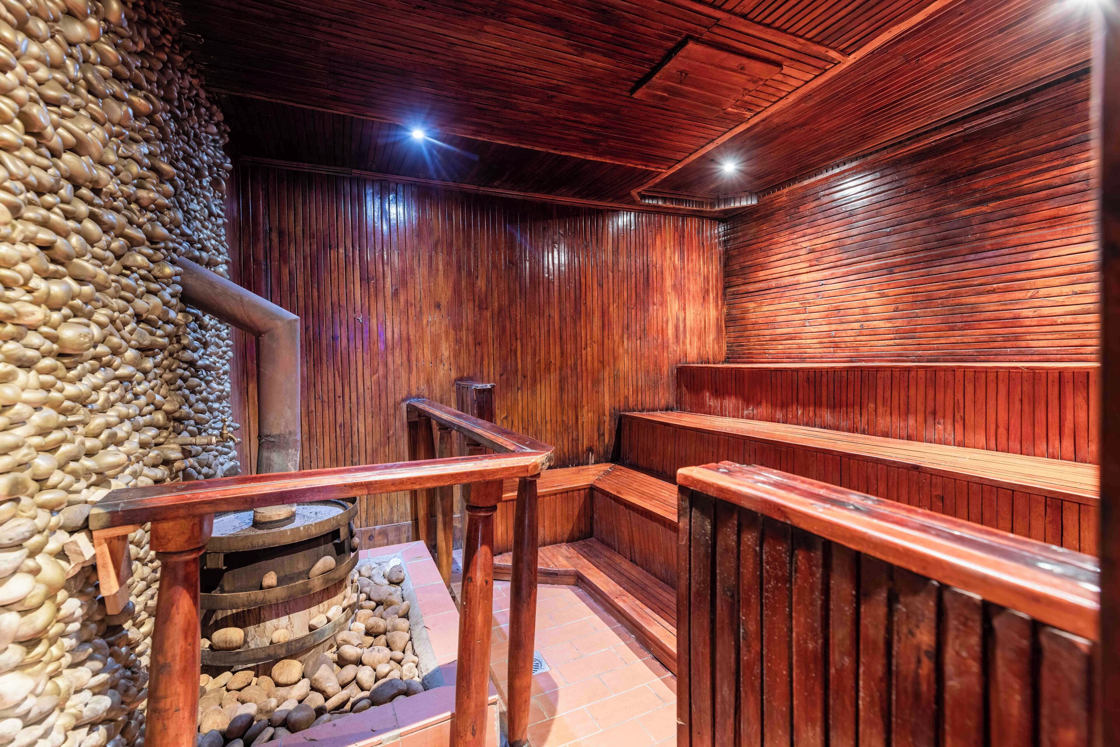 A sauna with wooden walls and benches, a stone wall on one side, and a wooden bench with a backrest in the center.