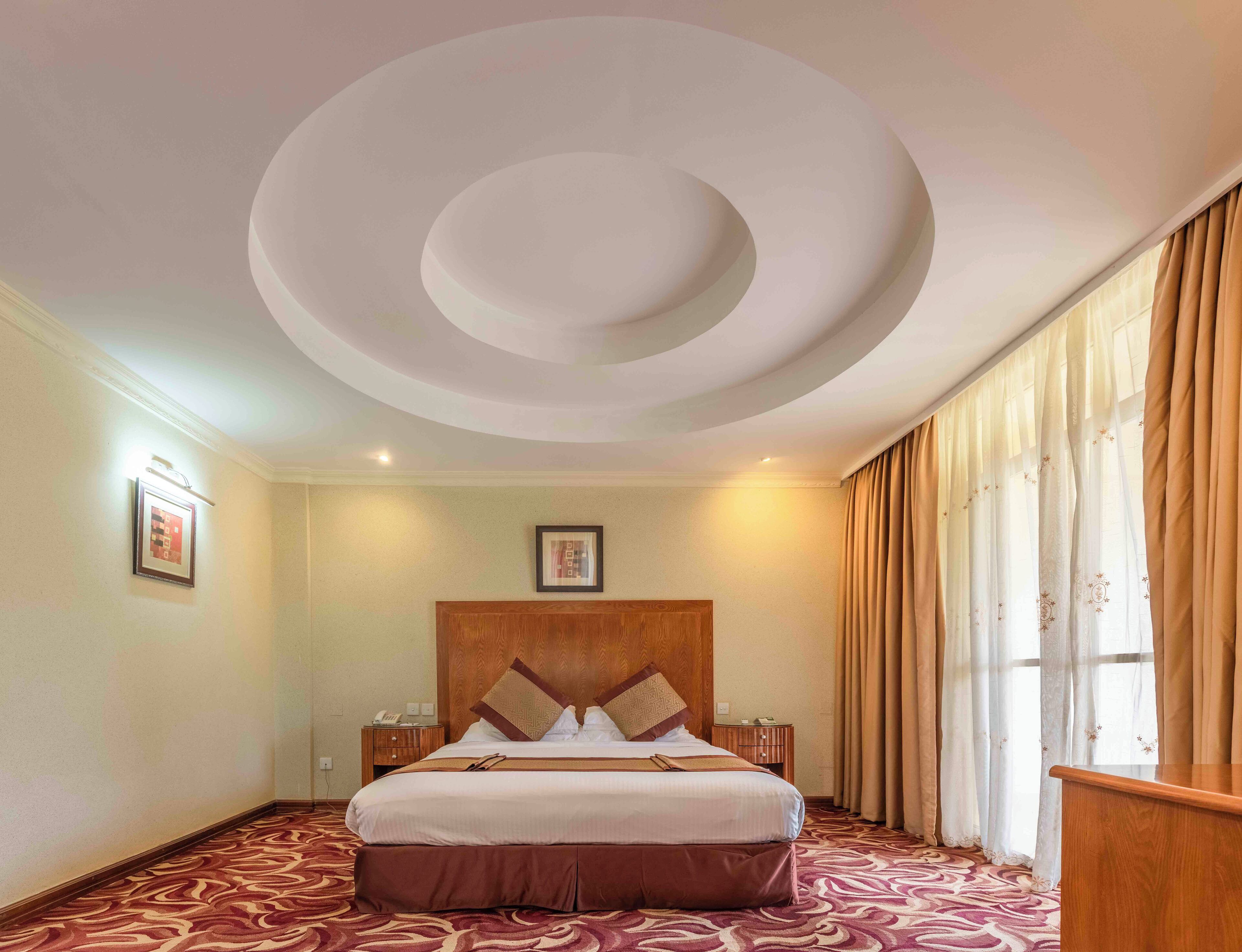 A hotel room with a large bed, a wooden headboard, a patterned carpet, and a circular ceiling design.