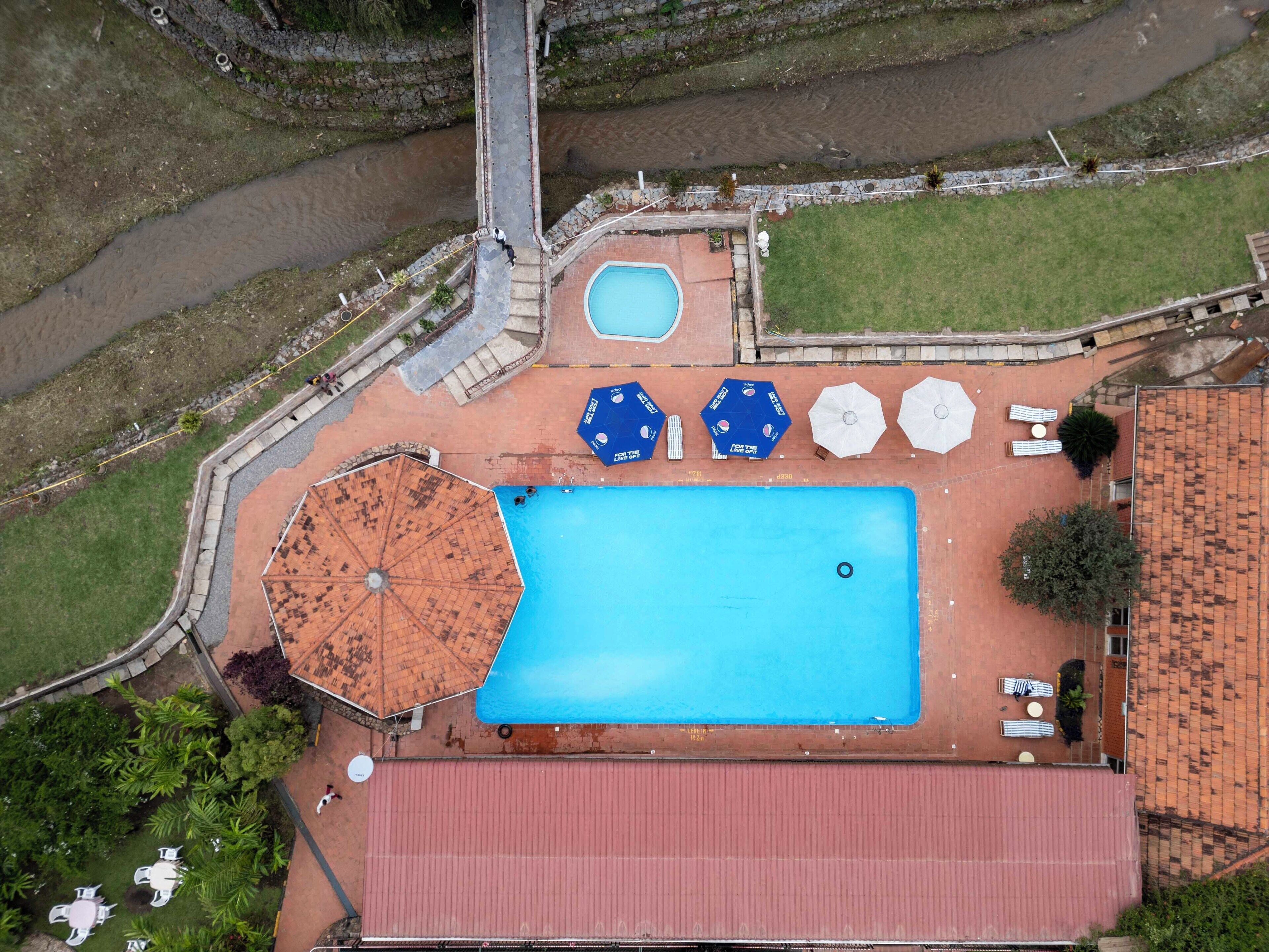 Vista aérea de uma área de piscina com um edifício de telhado vermelho, uma piscina pequena e vários guarda-sóis e espreguiçadeiras.