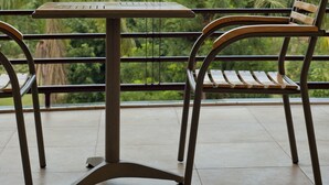 Een balkon met een tafel en twee stoelen, met uitzicht op een weelderig landschap met palmbomen en verre bergen.