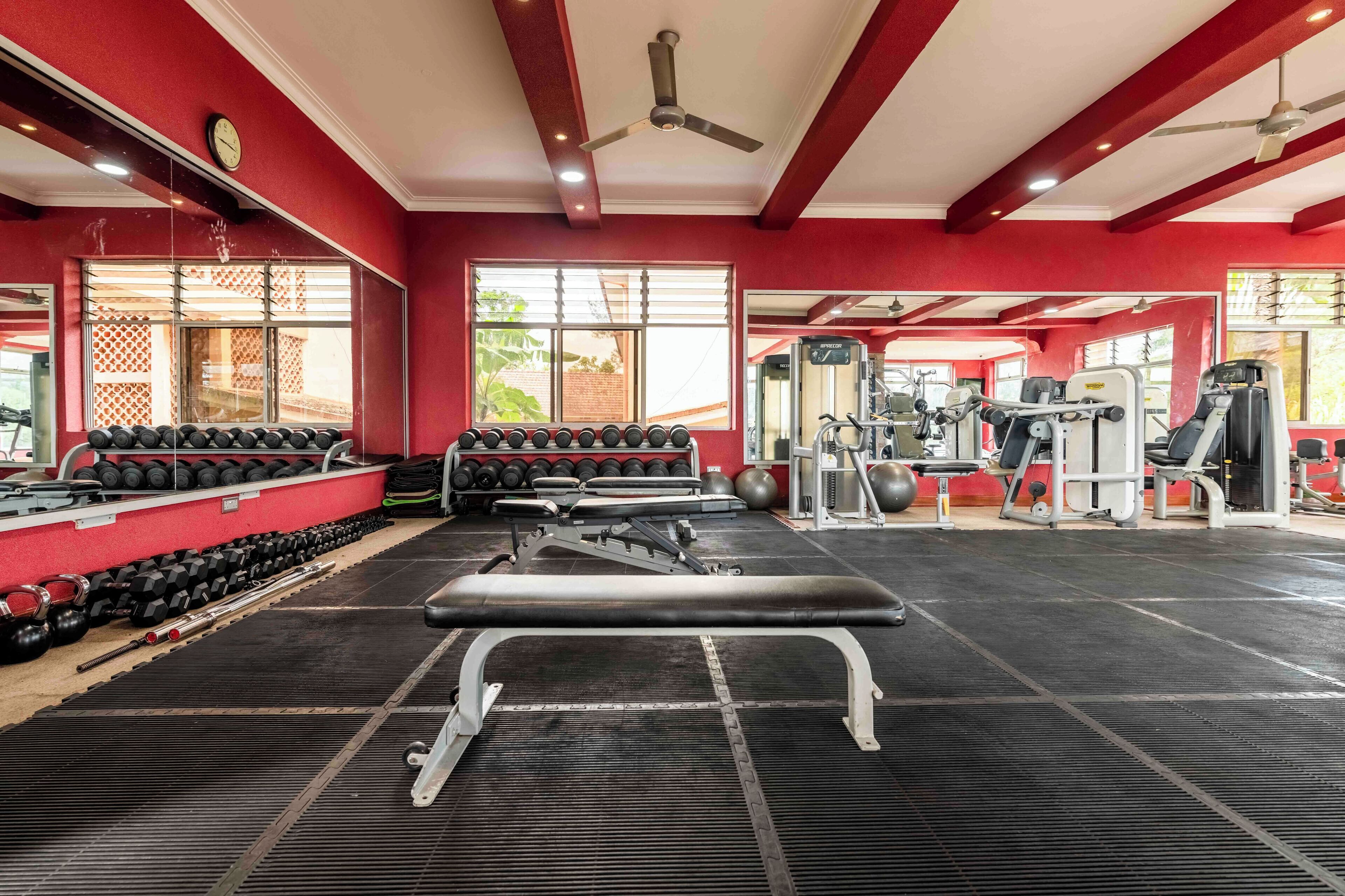 A gym with red walls, ceiling fans, and various exercise equipment including dumbbells, benches, and weight machines.