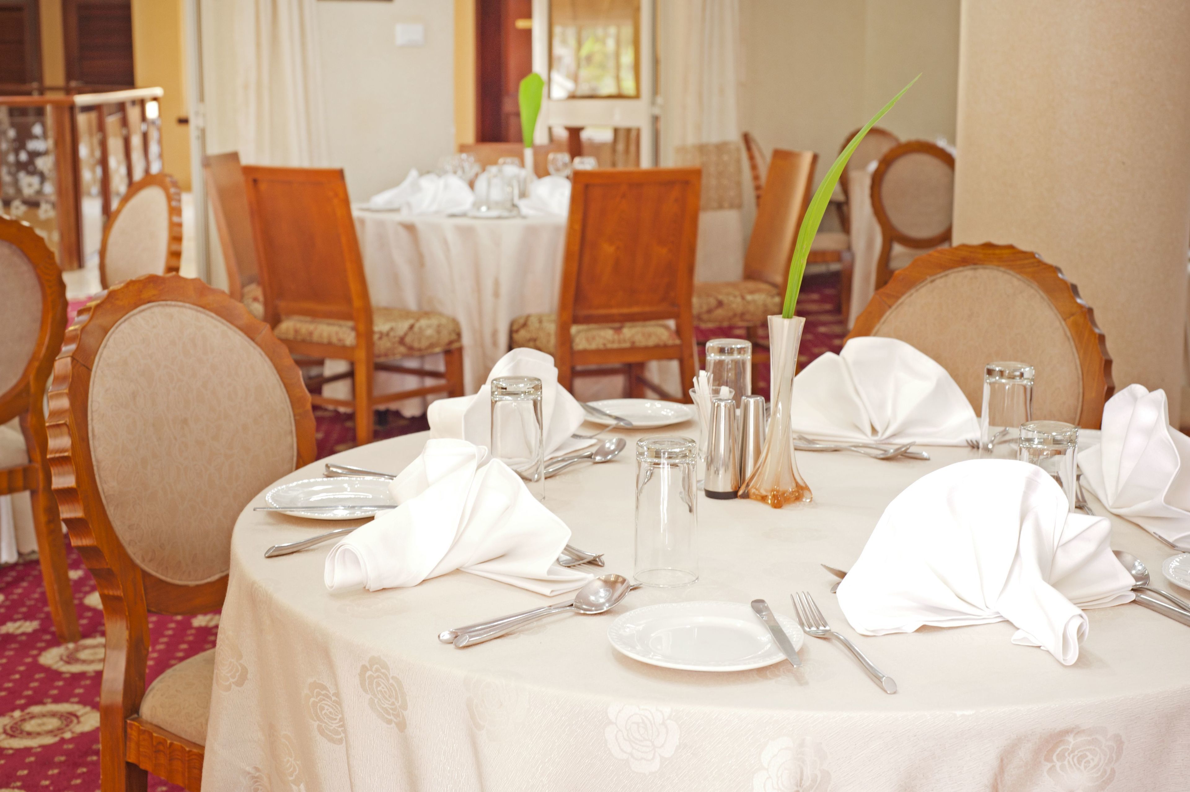 Mesa de comedor lista para cuatro personas, con manteles blancos, sillas de madera y cubiertos.