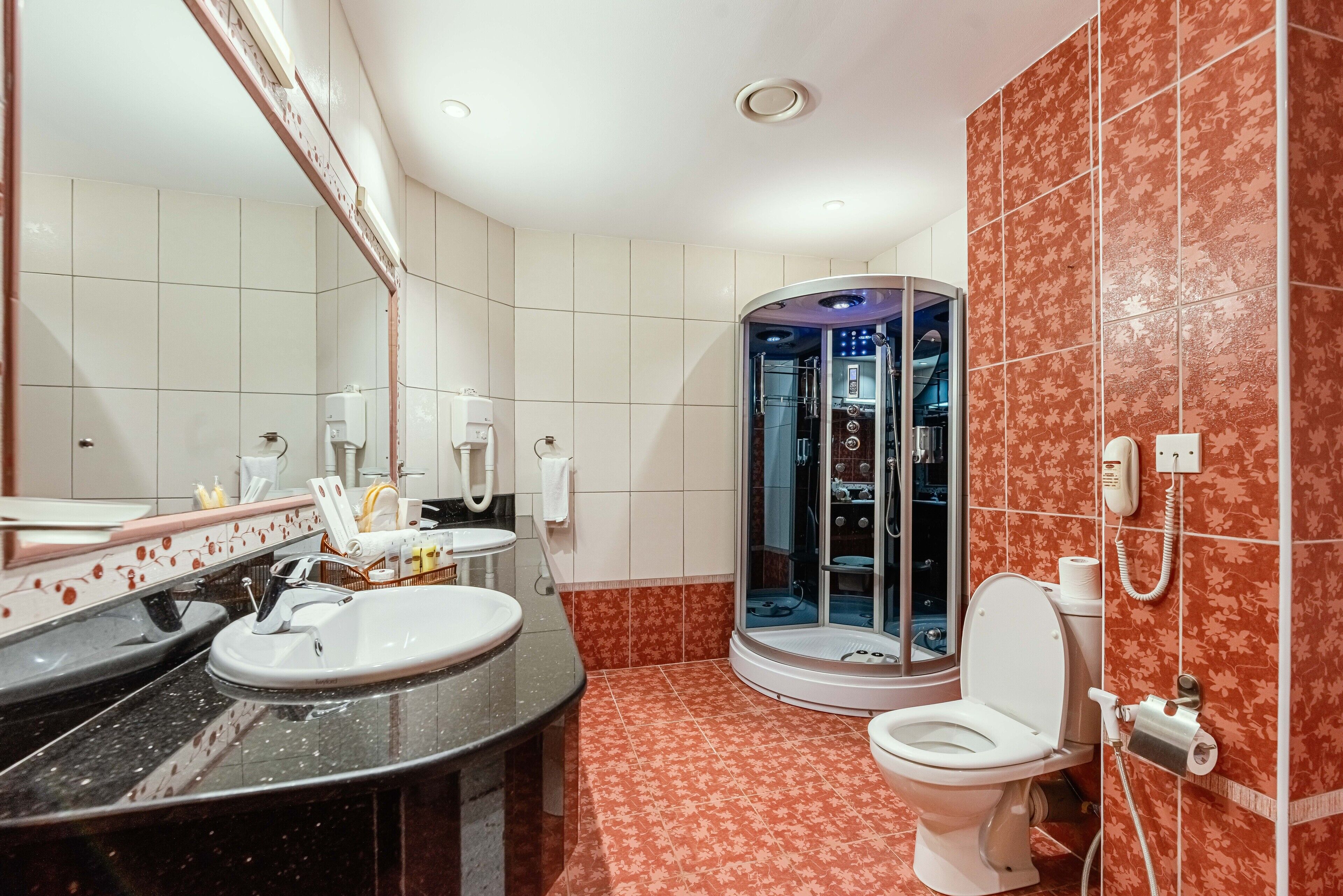 A bathroom with a curved shower, a toilet, and two sinks.