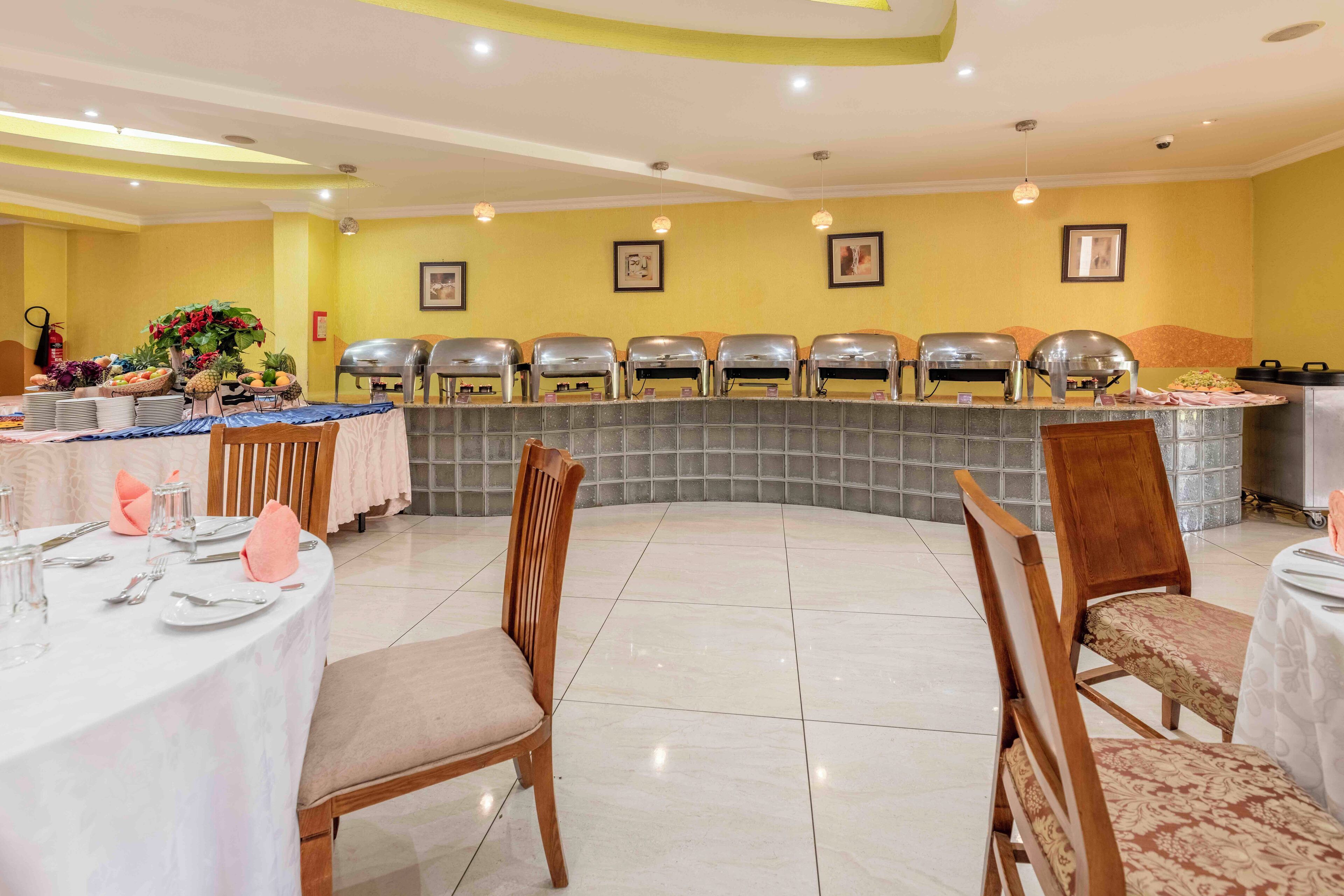 A dining area with round tables, chairs, and a buffet setup.