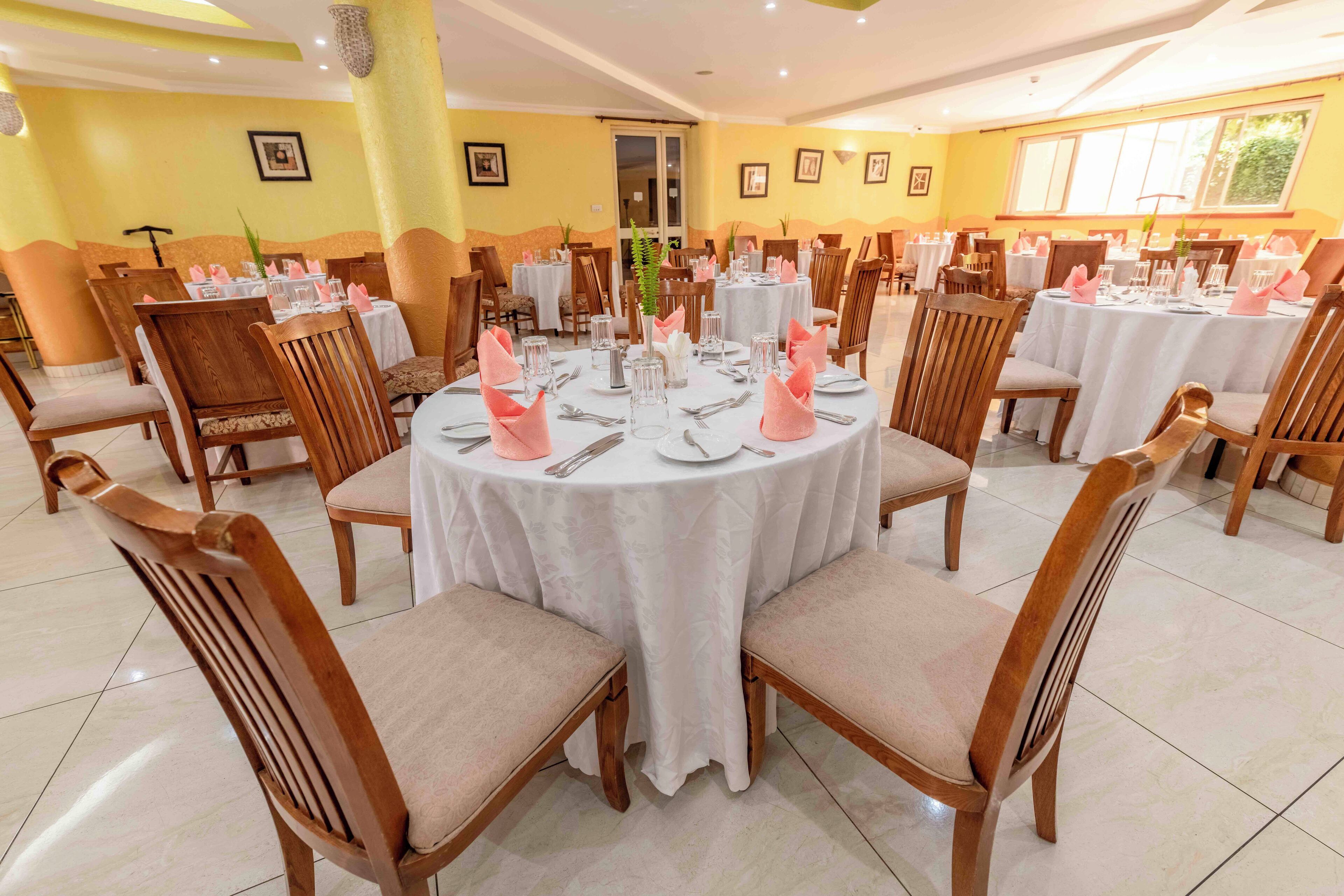 Un comedor con mesas redondas, sillas de madera y manteles blancos.